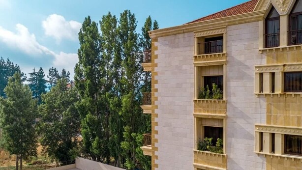 Un hôtel doté d’une piscine entourée de chaises longues, d’une façade en pierre et offrant une vue sur les arbres.