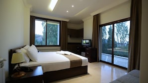 Une chambre d’hôtel avec un grand lit, une télévision, un bureau et un balcon donnant sur la verdure.