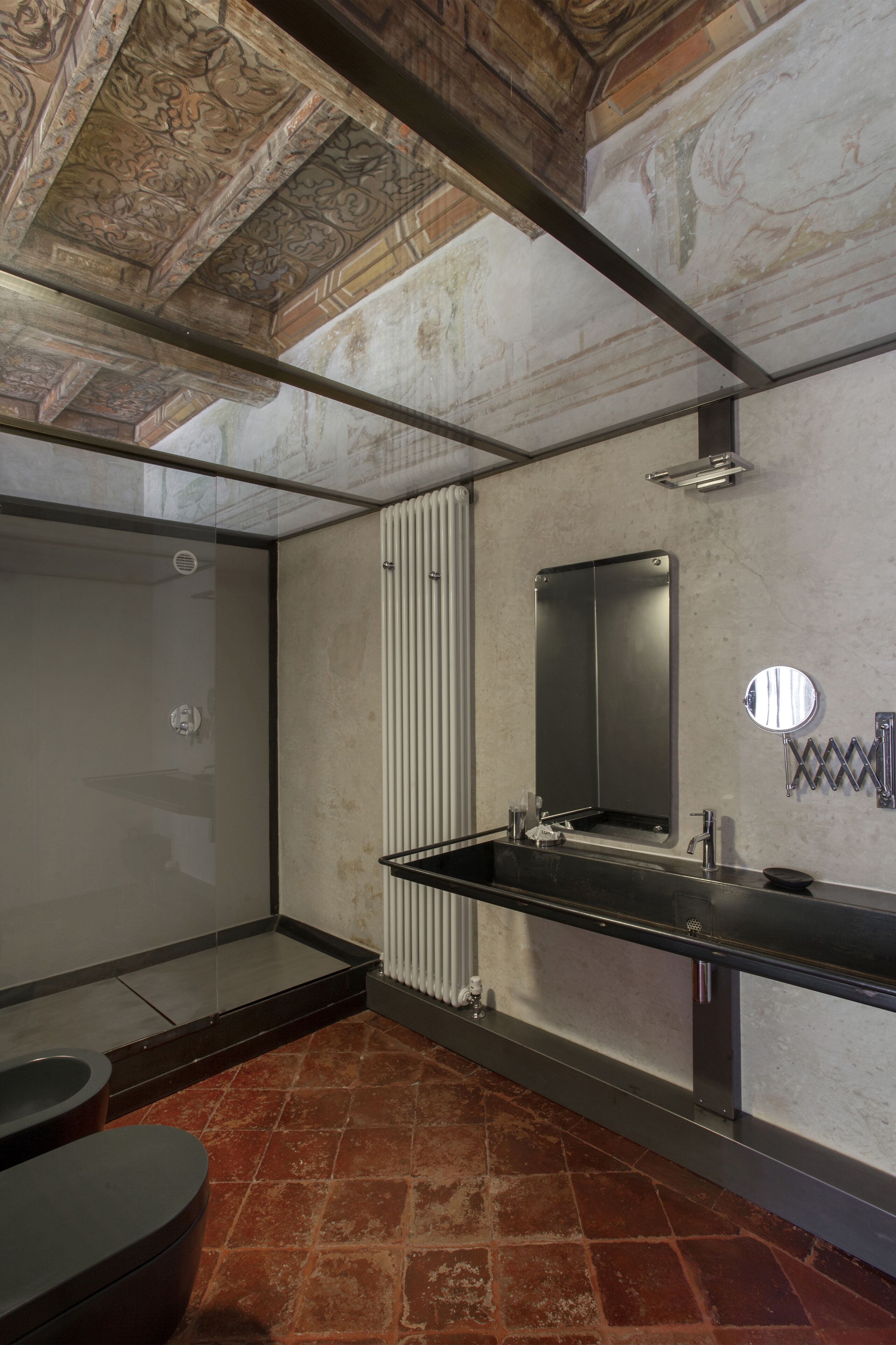 Un baño moderno con cabina de ducha de vidrio, un lavabo negro con espejo y suelo de baldosas rojas.