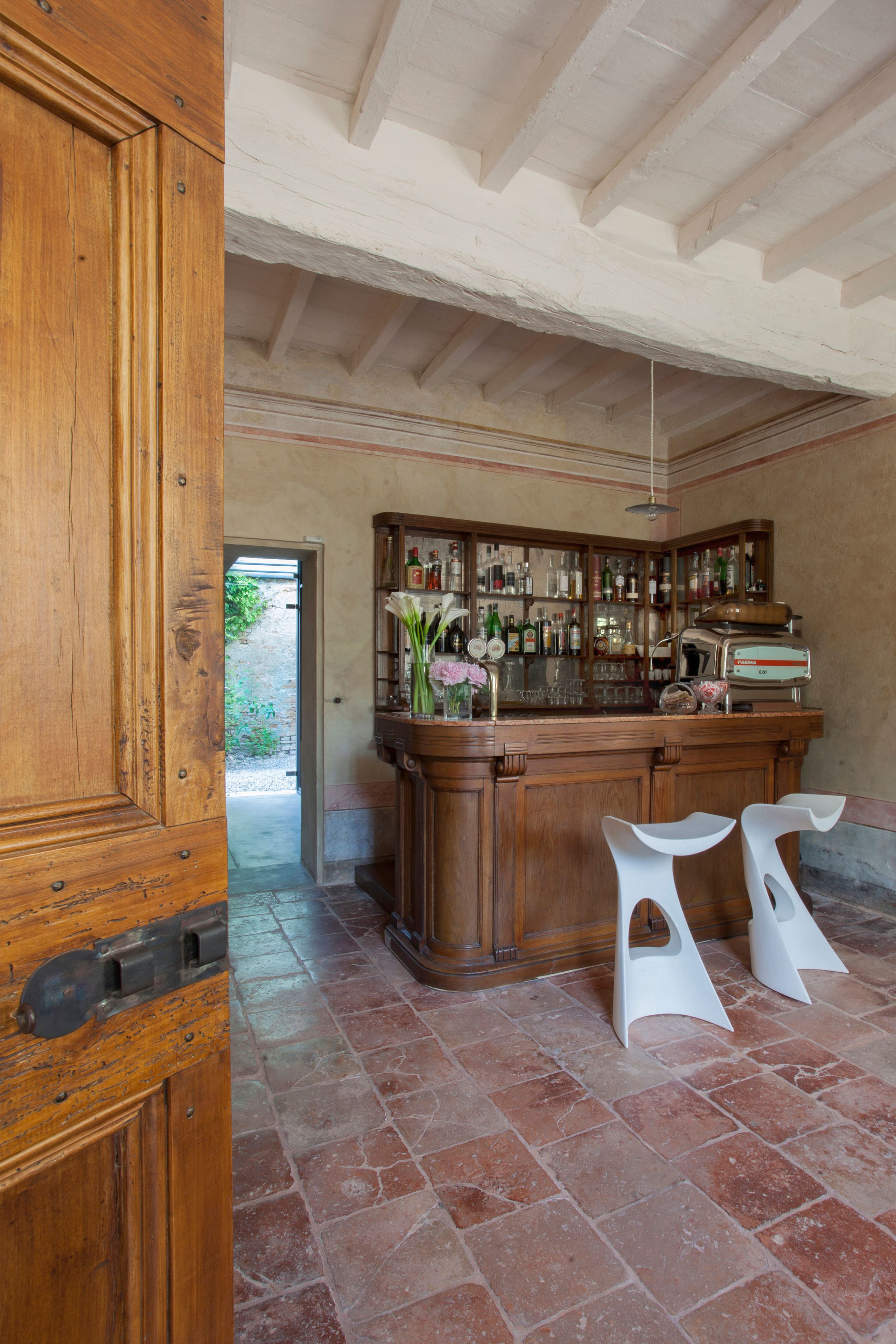 Zona de bar con mostrador de madera, taburetes blancos y una variedad de botellas y vasos.