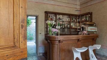 Zona de bar con mostrador de madera, taburetes blancos y una variedad de botellas y vasos.