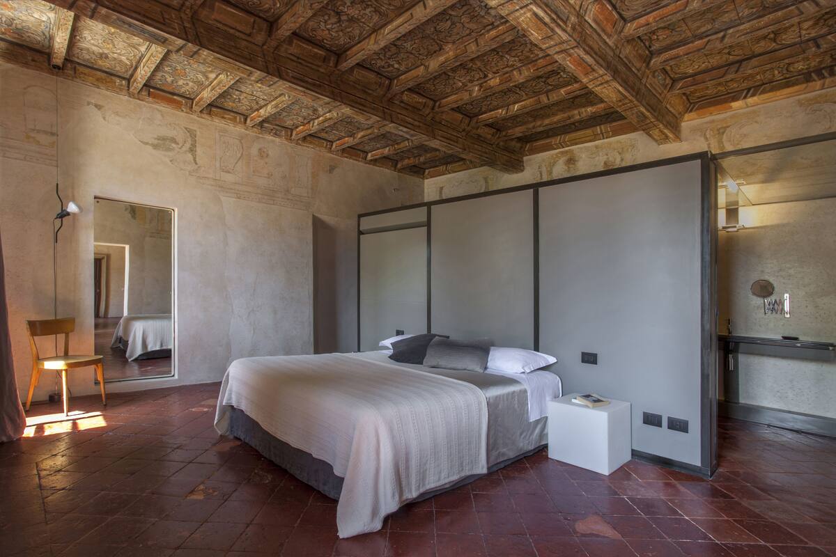 A bedroom with a large bed, a nightstand, a chair, and a mirror.