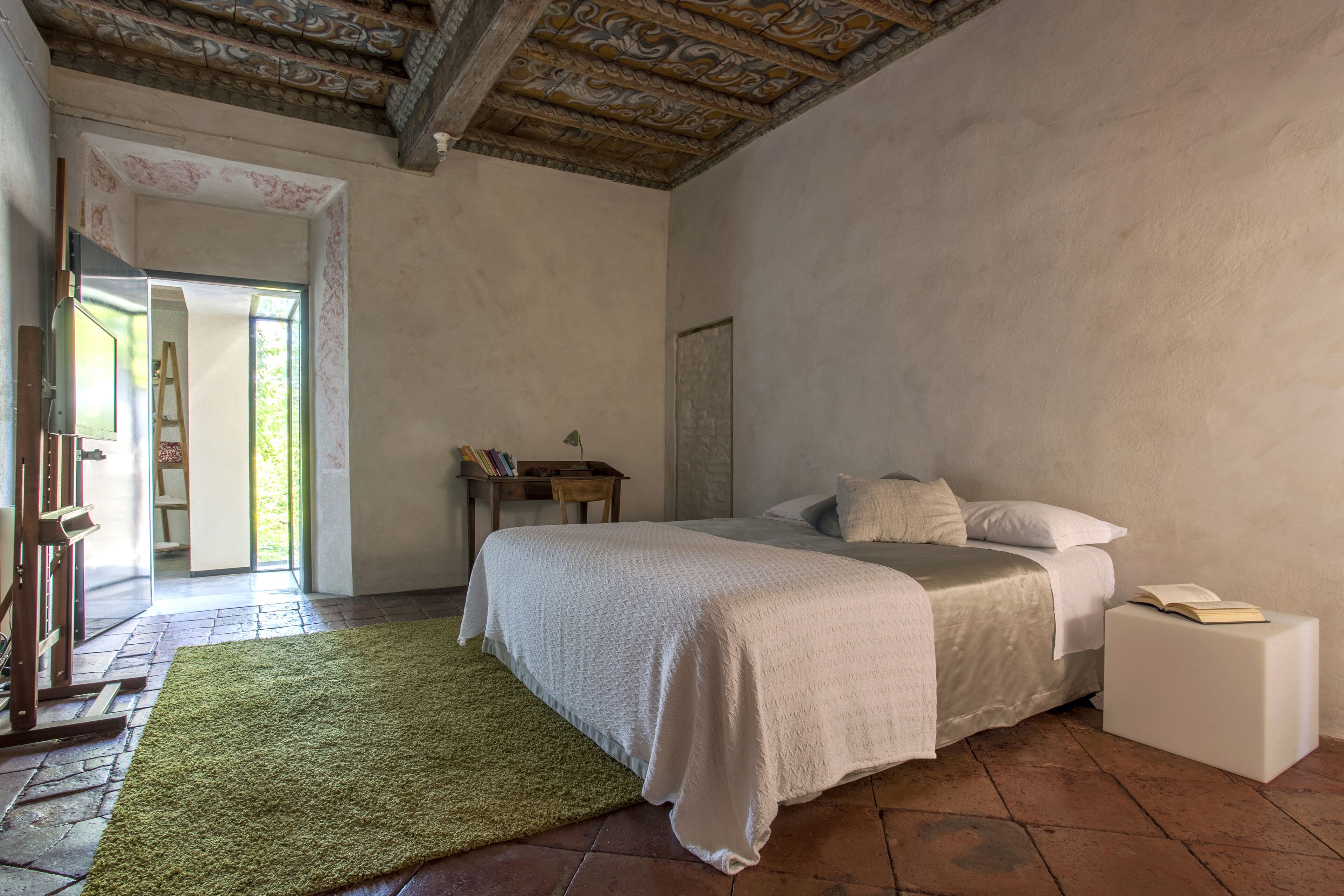 A bedroom with a bed, a green rug, a wooden side table, and a white bedside table.