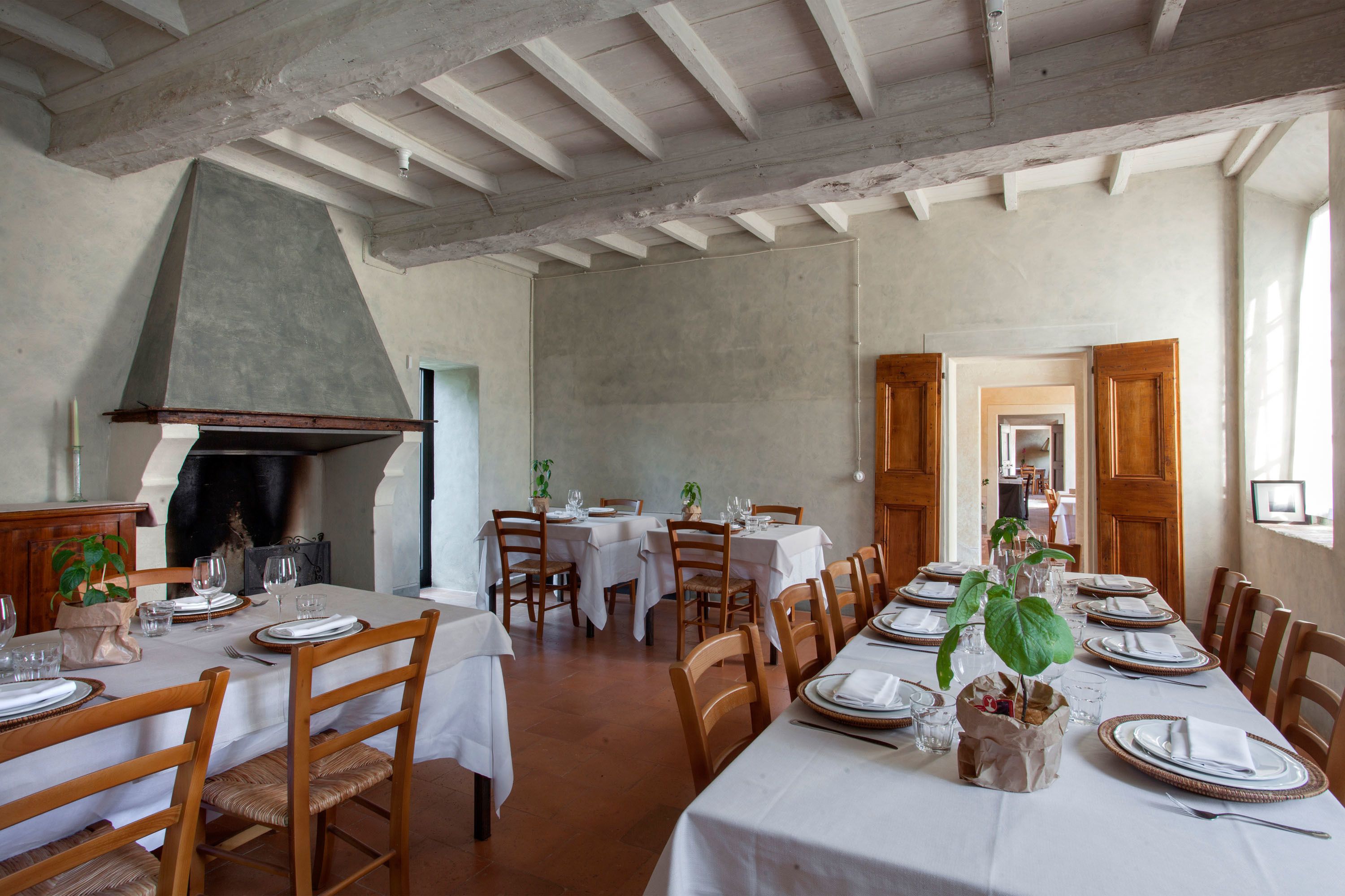 Un comedor con una mesa larga dispuesta para una comida, sillas de madera y una chimenea grande.