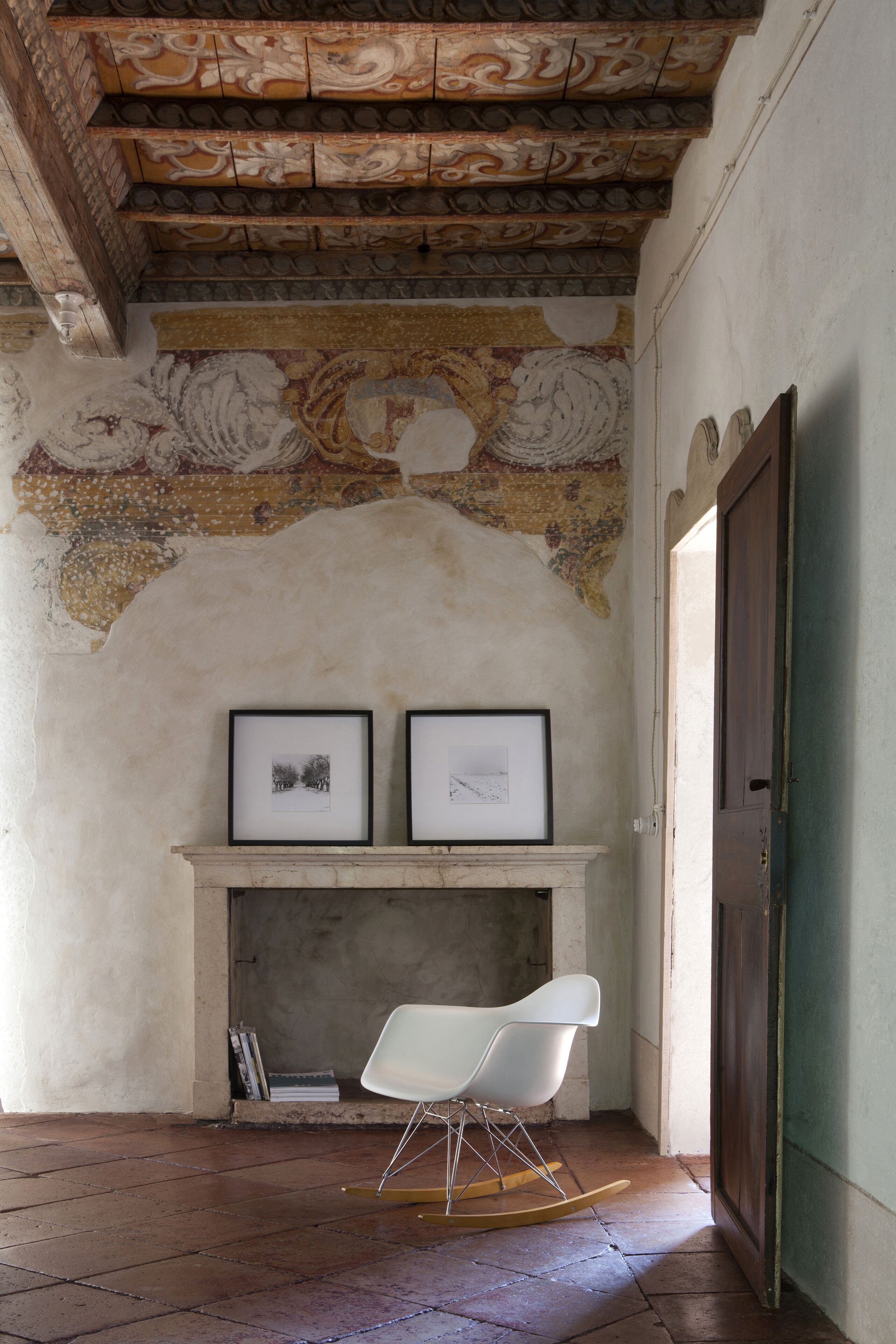 A room with a tiled floor, a white rocking chair, a fireplace, and a mural on the wall.