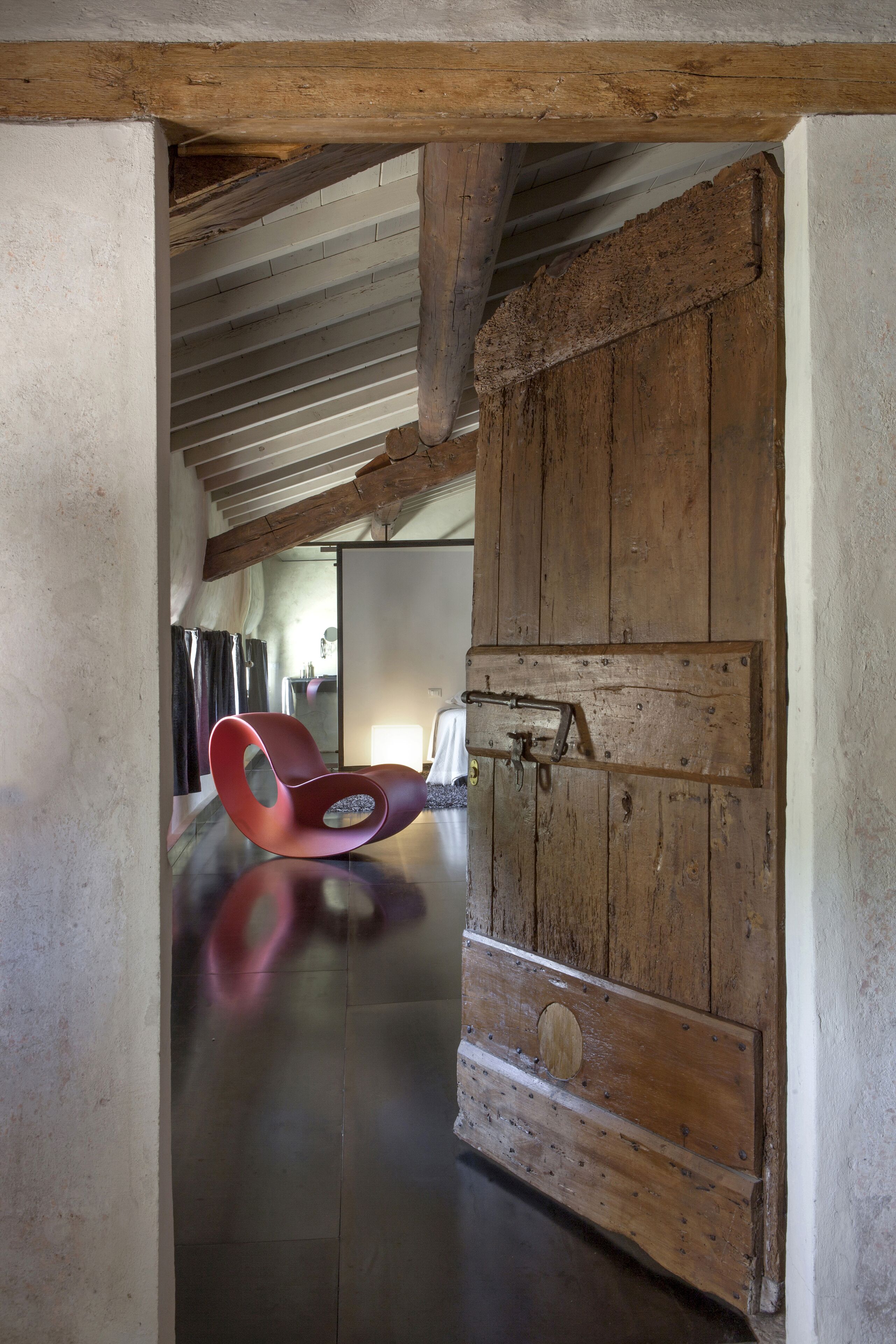 A rustic interior with exposed wooden beams, a large wooden door, and a red chair.