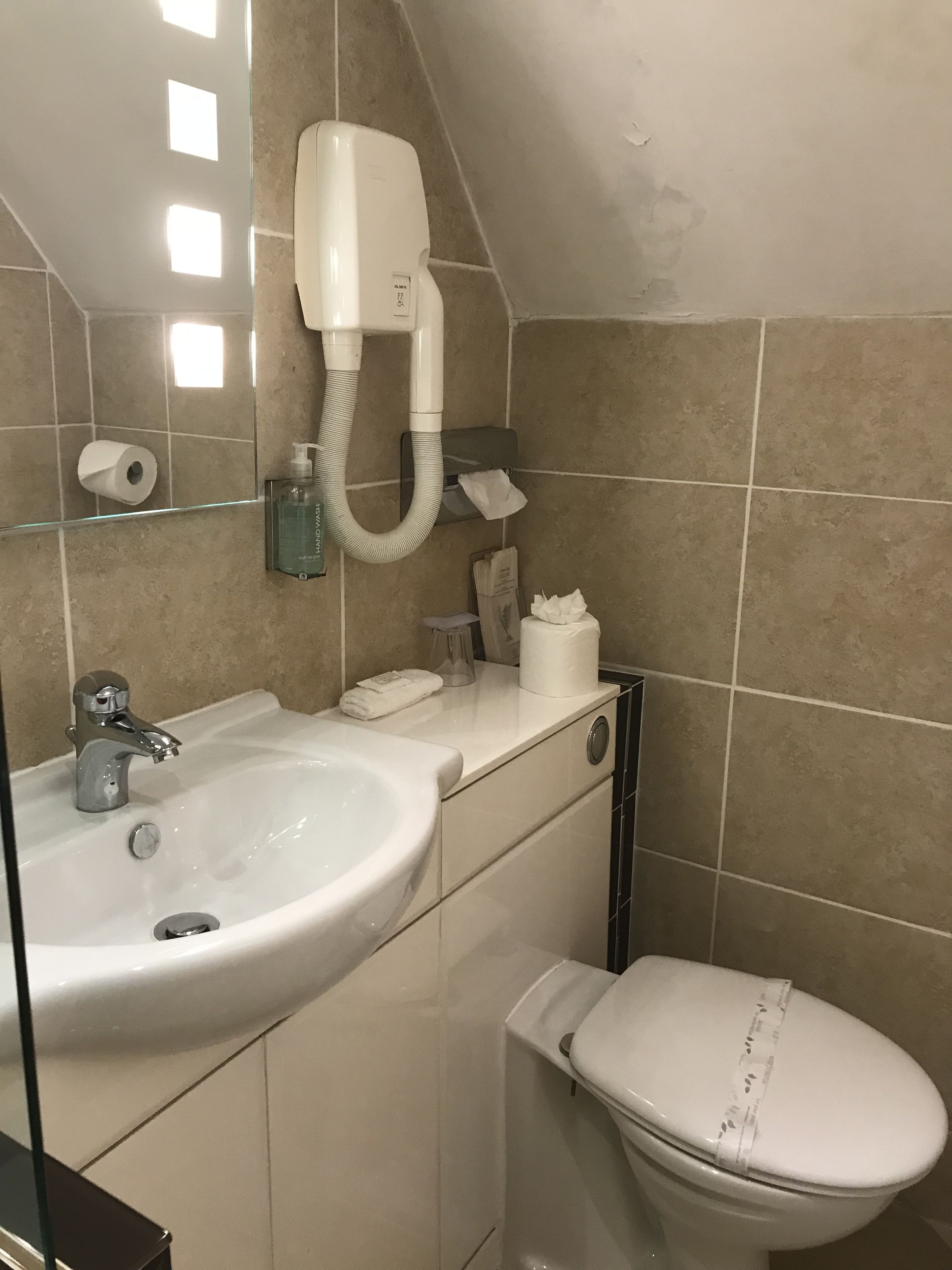Et badeværelse med vask, spejl, toilet og en hårtørrer fastgjort på væggen.