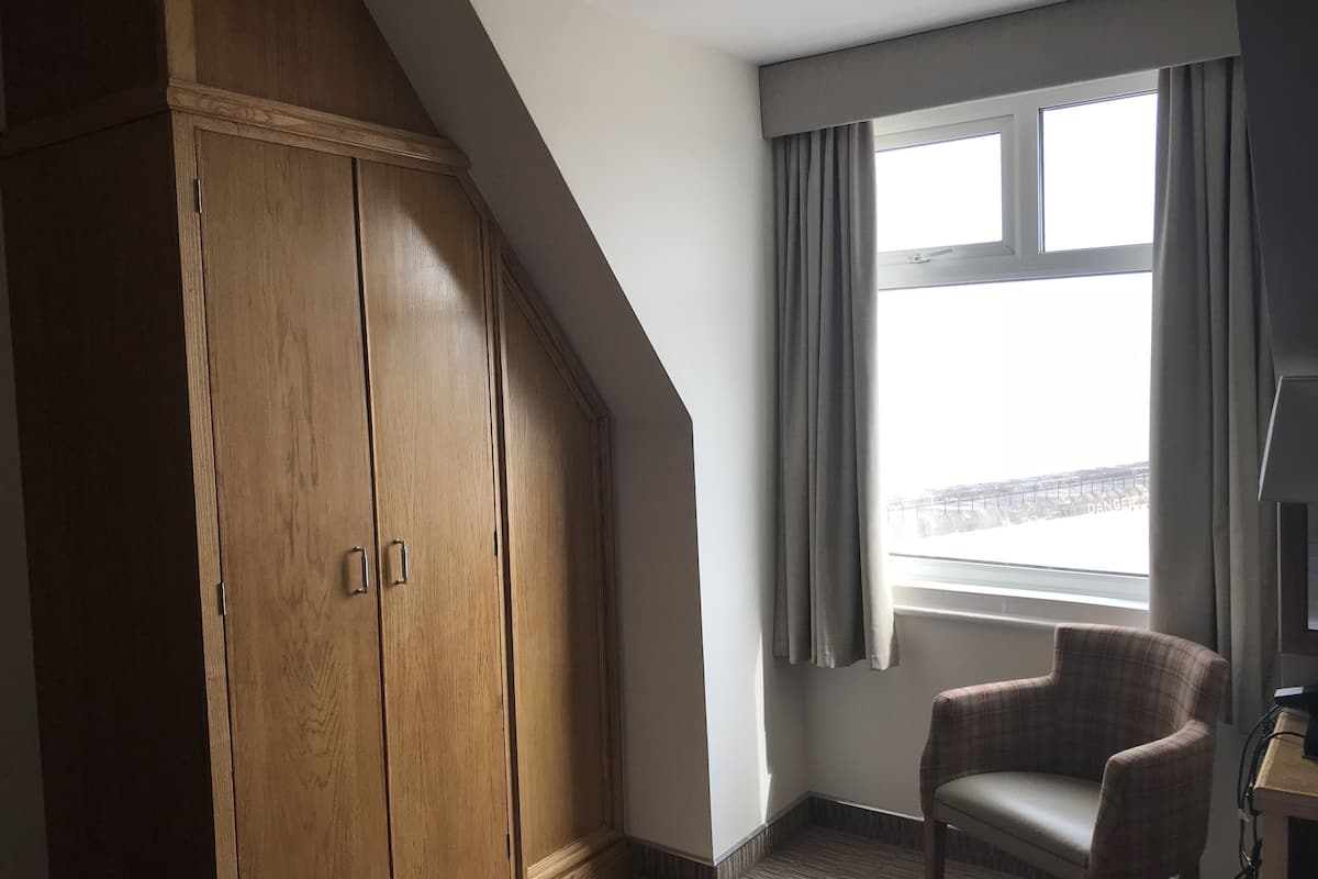 Une pièce avec une armoire en bois, un fauteuil à carreaux, une fenêtre avec des rideaux et une vue sur un pont.