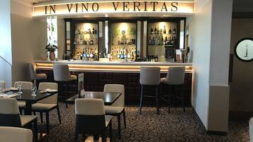 A bar area with a sign reading "IN VINO VERITAS" and a variety of bottles on shelves. There are several tables and chairs arranged for seating.