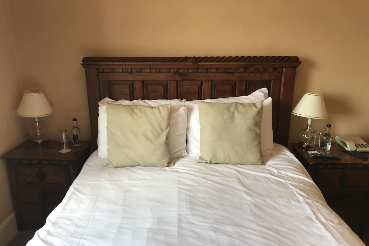 Un lit bien fait, avec deux oreillers, une tête de lit en bois et des tables de chevet équipées de lampes et d’un téléphone.