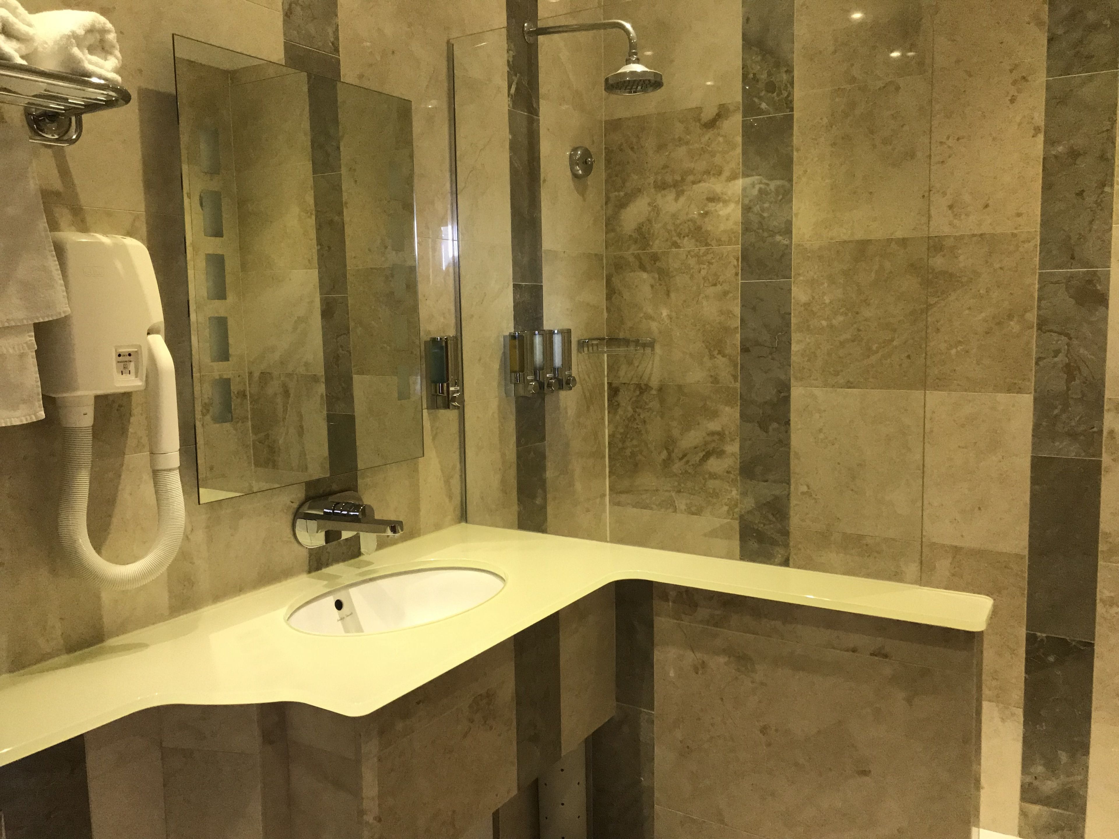 Un bagno moderno con parete in marmo, lavandino, cabina doccia in vetro e porta asciugamani.