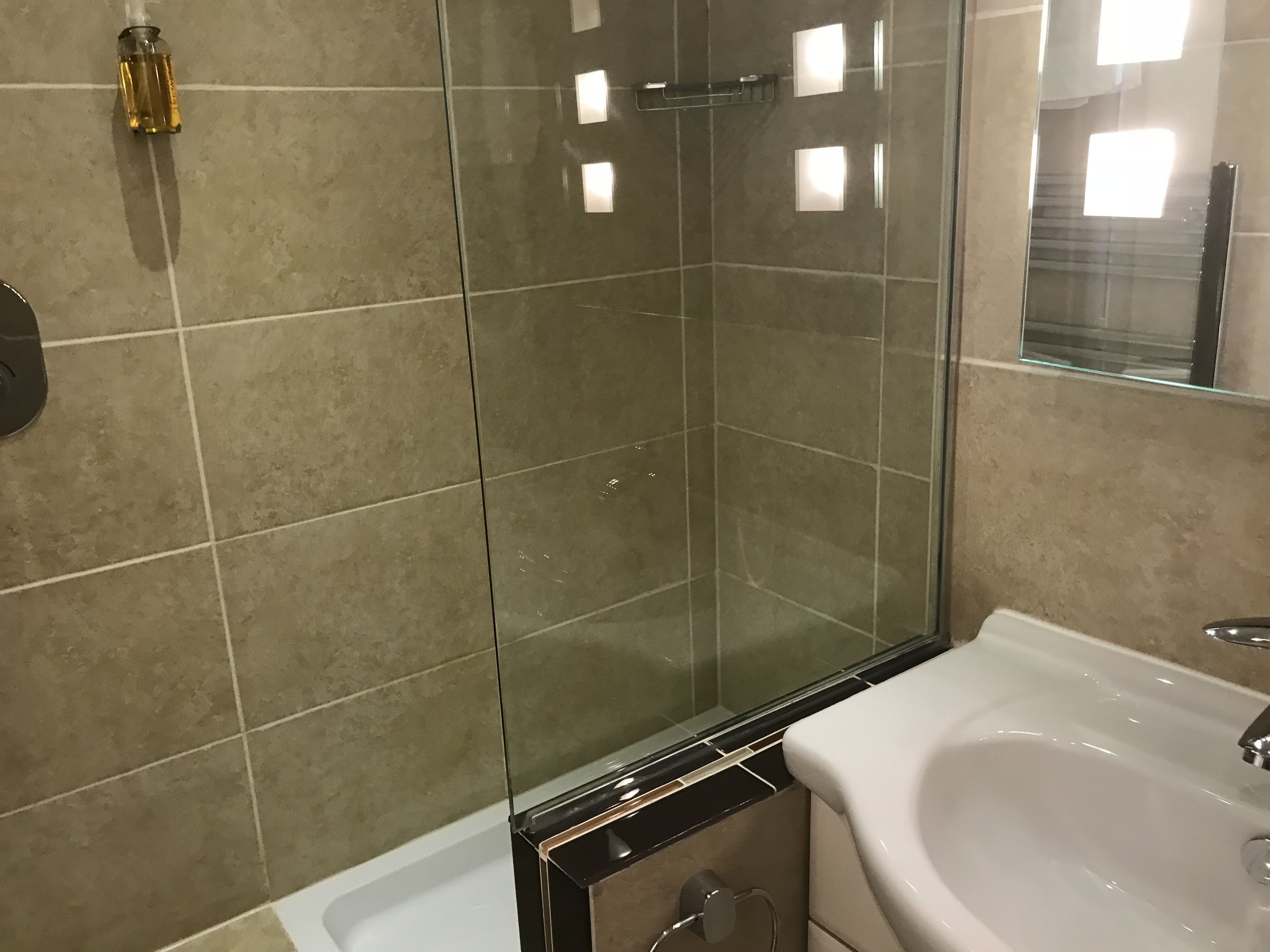 A bathroom with a glass shower enclosure, a white sink, and beige tiles.