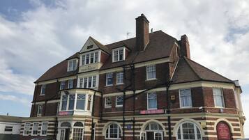 A multi-story hotel with a classic design, featuring a prominent 'Pier Hotel' sign, a pub named 'Rub on the Pier', and a car parked in front.