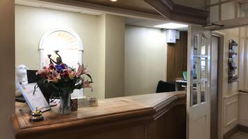 A reception desk with a vase of flowers, a bell, and a sign indicating the reception is unattended.