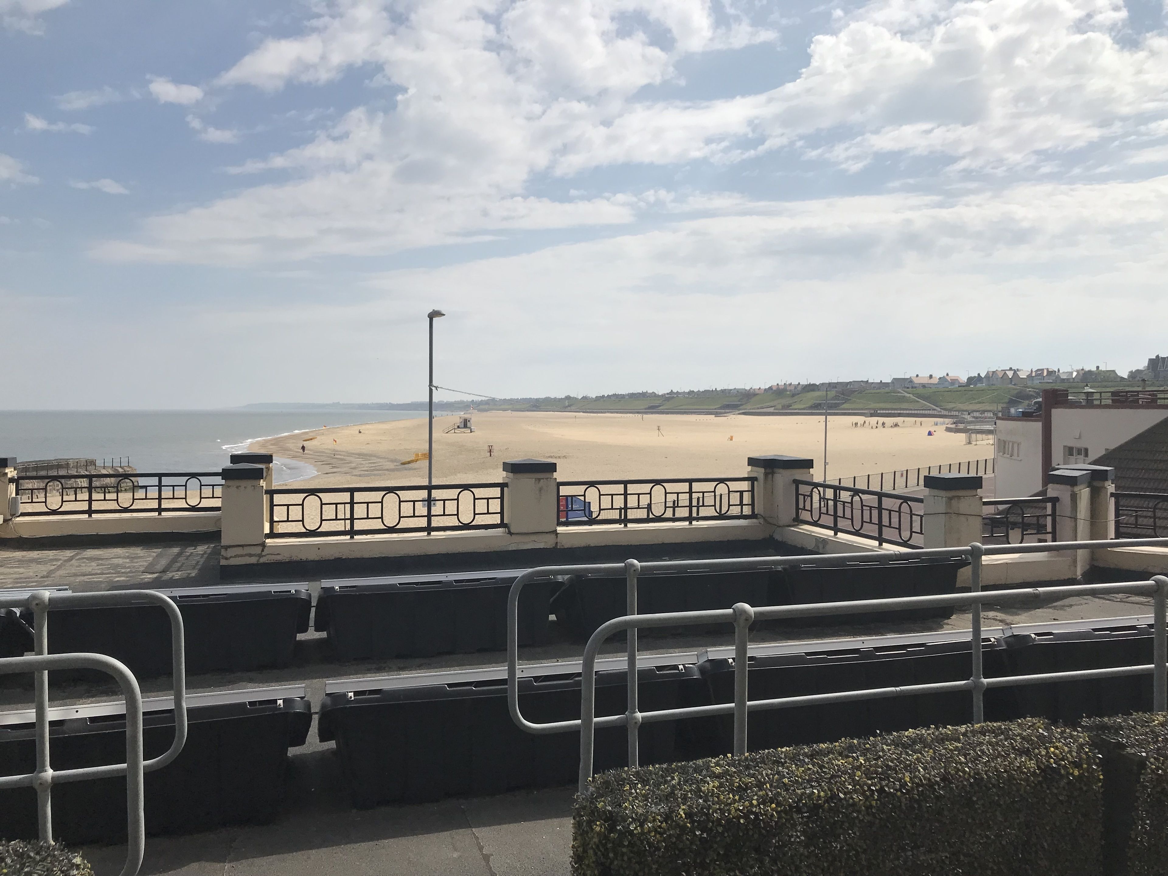Vista da praia a partir de uma varanda com guarda-corpo, uma torre salva-vidas e céu claro.
