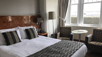A hotel room with a large bed, a small table, two chairs, a lamp, and a window with curtains.