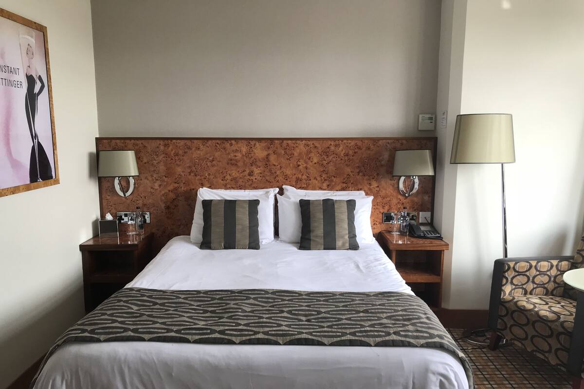 Une chambre d’hôtel avec un grand lit, deux tables de chevet, une chaise et une lampe.