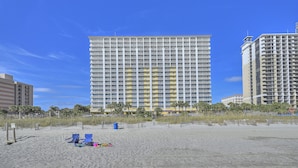 A high-rise hotel with multiple balconies, situated on a sandy beach with a clear blue sky. - Camelot by the Sea by Elliott Beach Rentals (Myrtle Beach)
