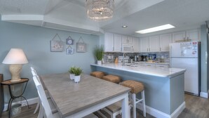 A modern kitchen with white cabinetry, a central island, and a chandelier. - Camelot by the Sea by Elliott Beach Rentals (Myrtle Beach)