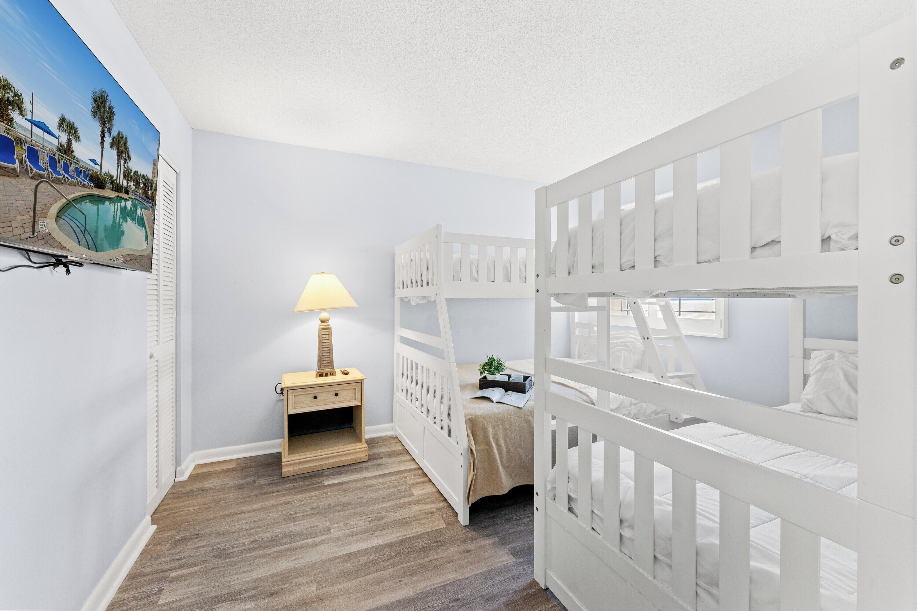 A child's room with bunk beds, a nightstand, a lamp, and a wall-mounted picture.
