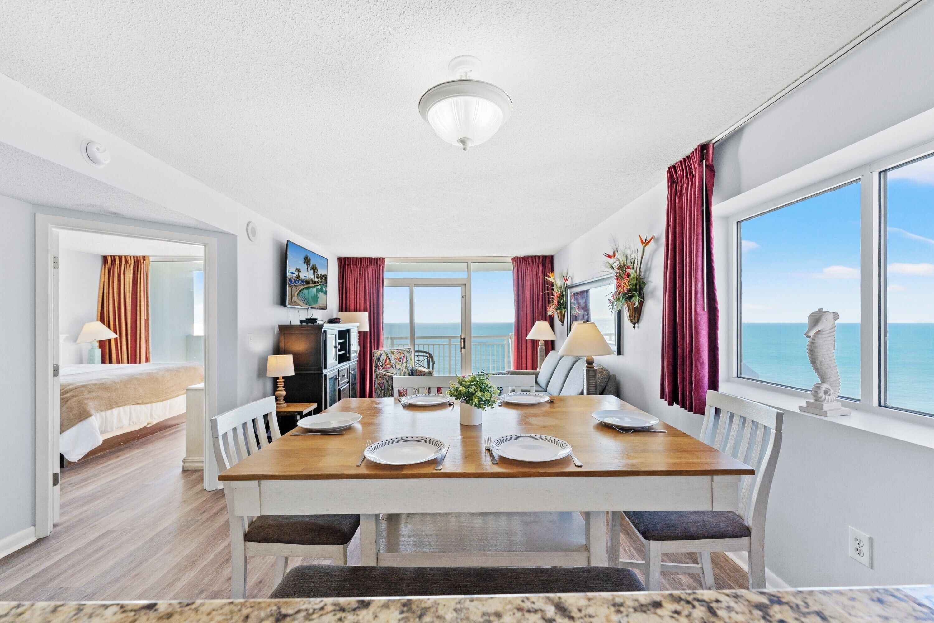 A hotel room with a dining area, a bed, a TV, and a view of the sea.