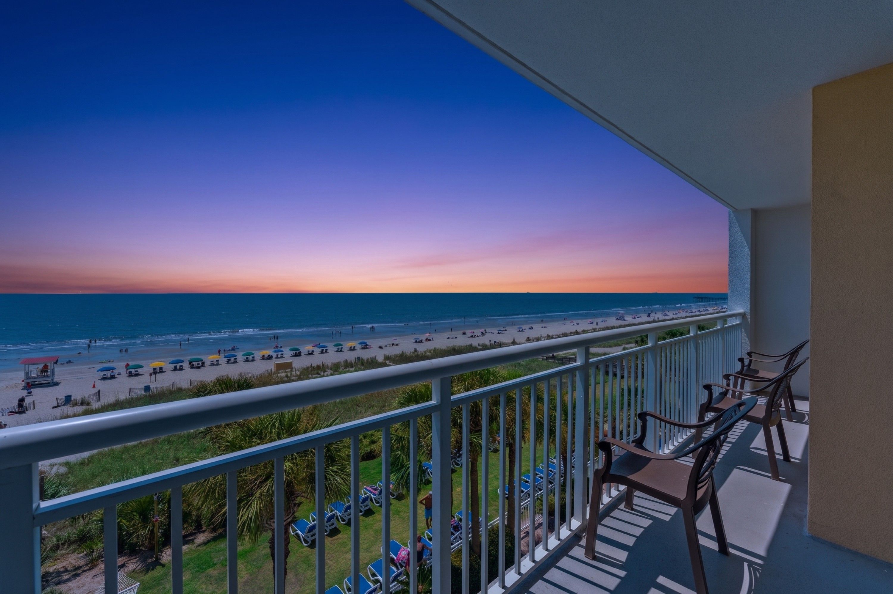 A balcony with a view of a beach and ocean during sunset.