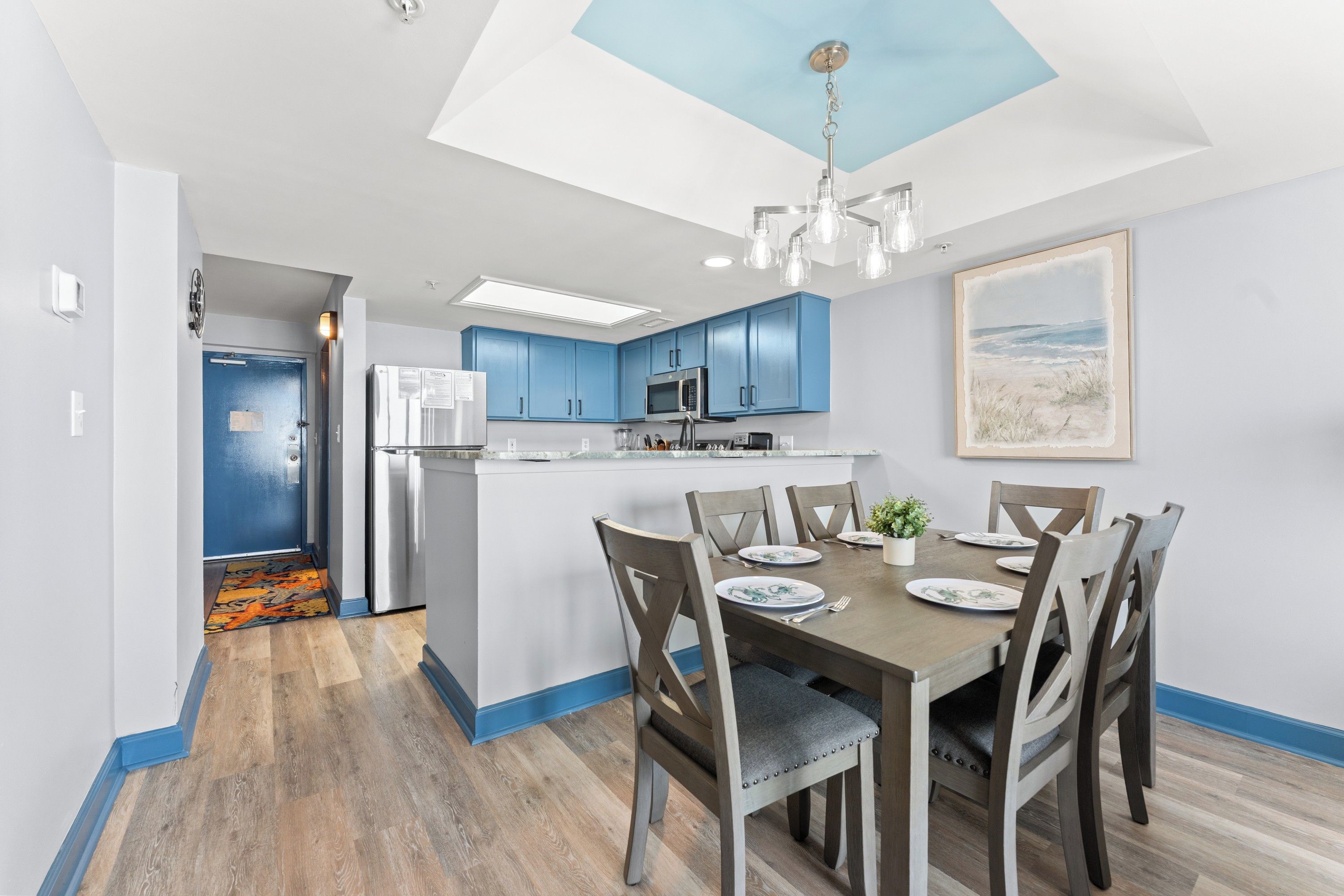 Una cocina moderna con armarios azules, una isla central y un comedor con seis sillas y una mesa dispuesta para cuatro.