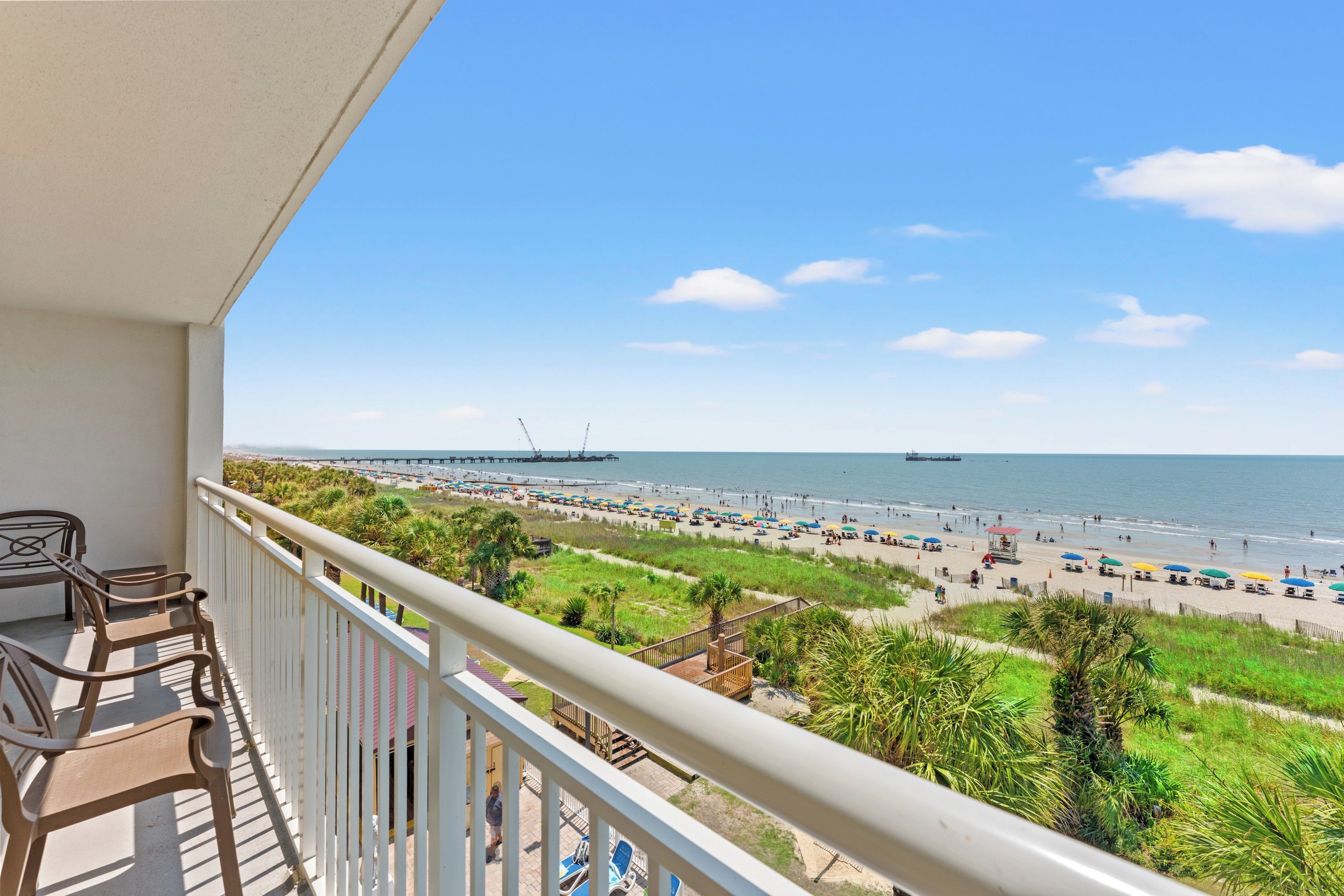A balcony with a view of a beach, a pier, and a ship in the distance.