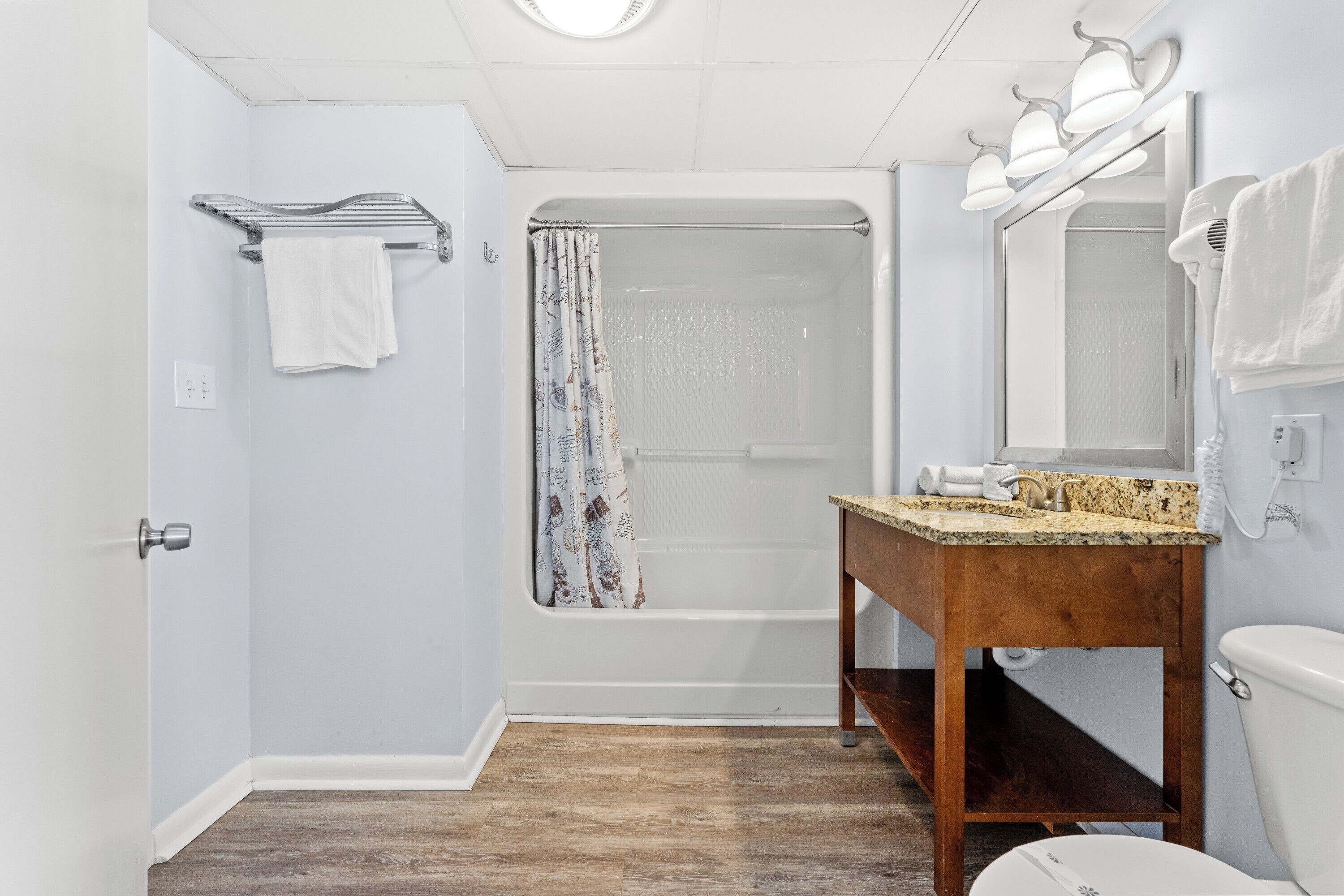 A bathroom with a shower, toilet, vanity, and towel rack.