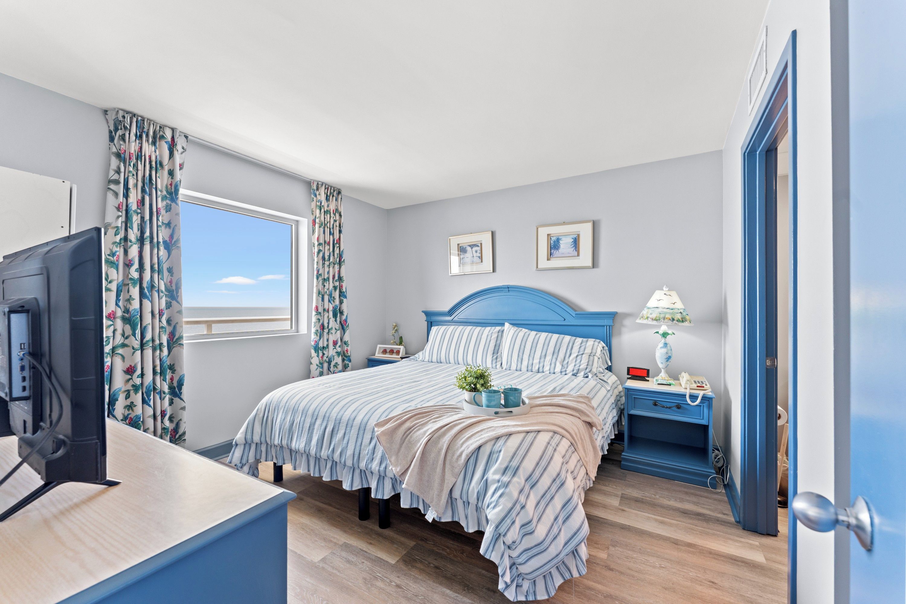 A bedroom with a bed, a bedside table, a lamp, a TV, and a window with curtains.
