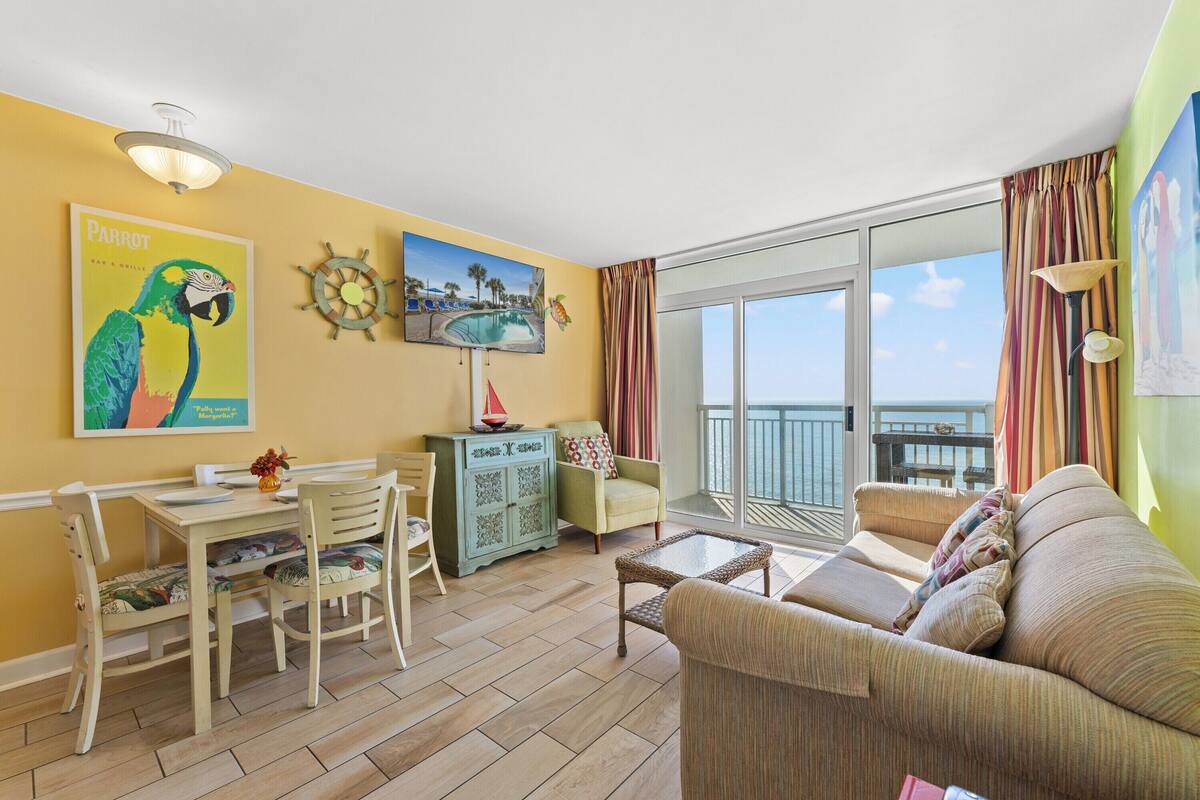 Un salon comprenant une table à manger, des chaises, un canapé, un balcon avec vue et des œuvres d’art accrochées aux murs.