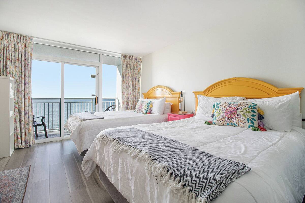 Une chambre d’hôtel avec deux lits, un balcon avec une chaise et une vue sur la mer.