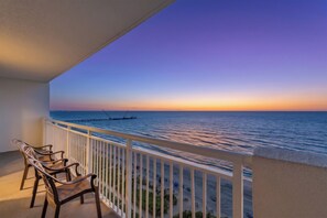 A balcony with a view of the sea at sunset, wooden chairs, and a white railing. - Camelot by the Sea by Elliott Beach Rentals (Myrtle Beach)