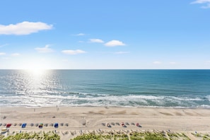 A beach with a clear sky, ocean waves, and beachgoers. - Camelot by the Sea by Elliott Beach Rentals (Myrtle Beach)