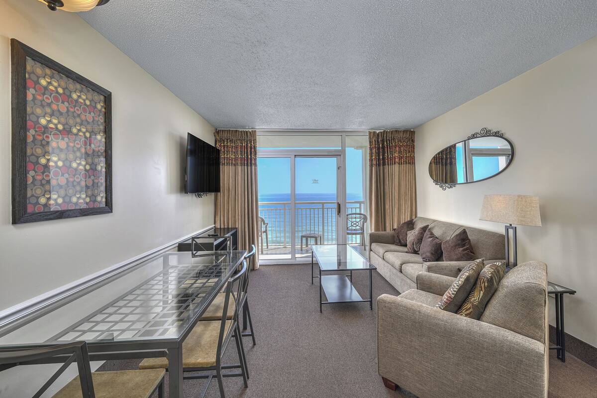 Une chambre d’hôtel avec un balcon, une table à manger, un canapé et un téléviseur.