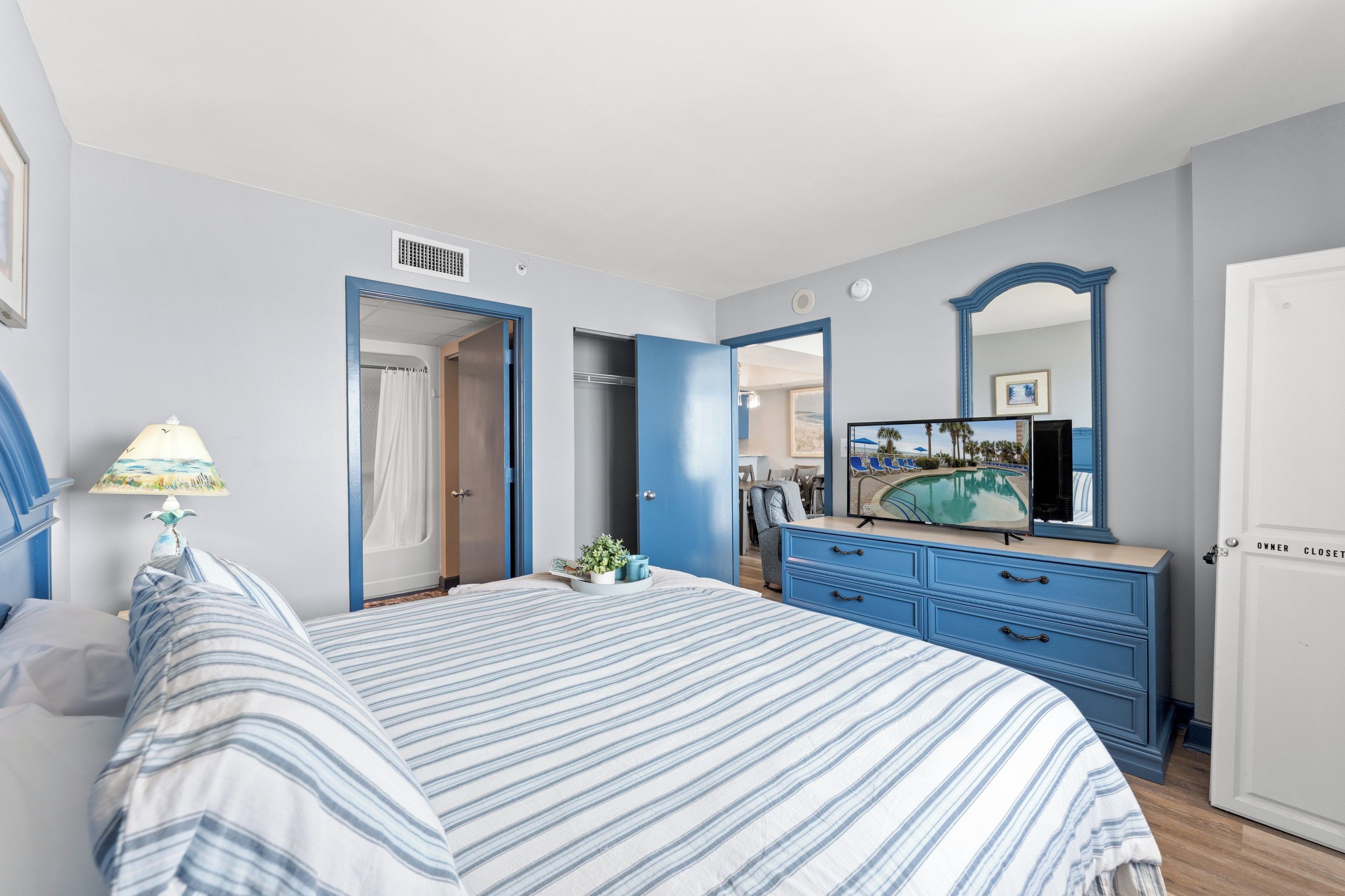 A bedroom with a bed, a dresser, a mirror, and a door leading to a bathroom.