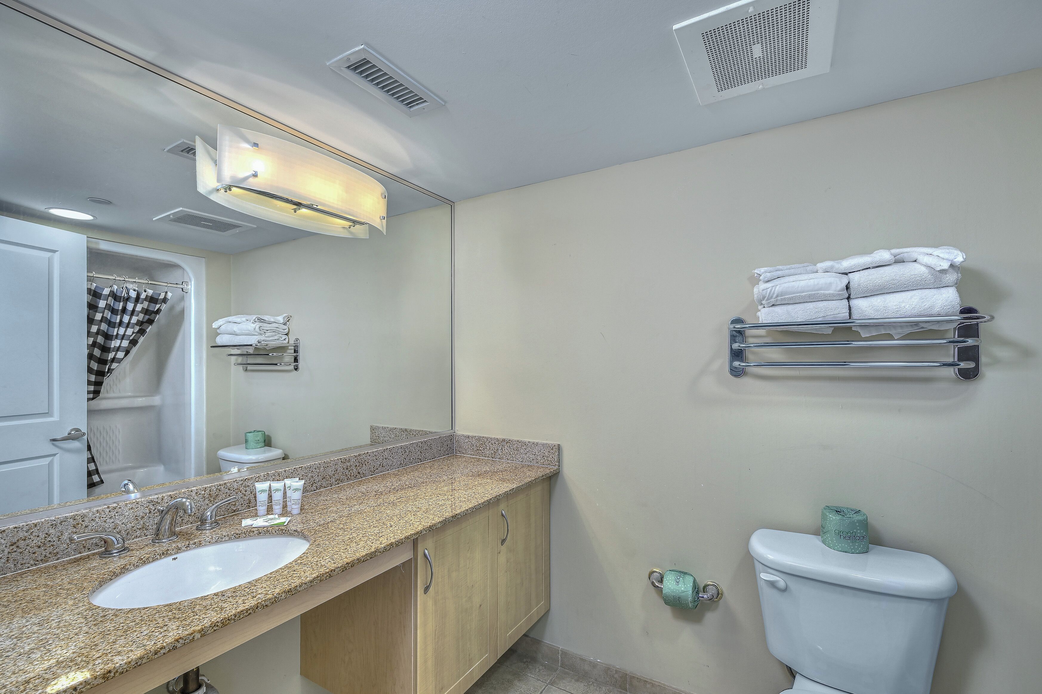 A bathroom with a sink, mirror, towel rack, toilet, and shower curtain.
