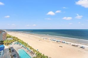 A beach resort with a swimming pool, beach umbrellas, and a pier extending into the ocean. - Units at Sandy Beach Resort by Elliott Beach Rentals (Myrtle Beach)