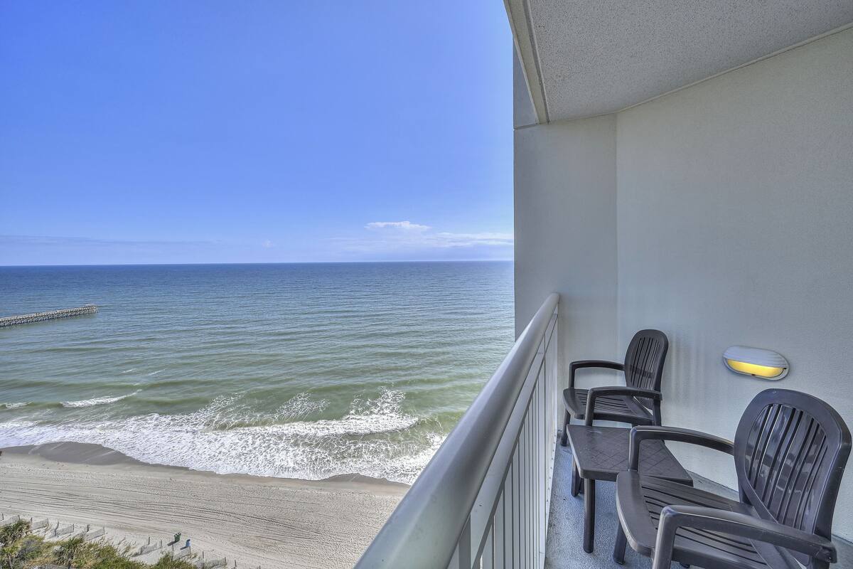 A balcony with a view of the ocean, featuring two chairs and a small table.