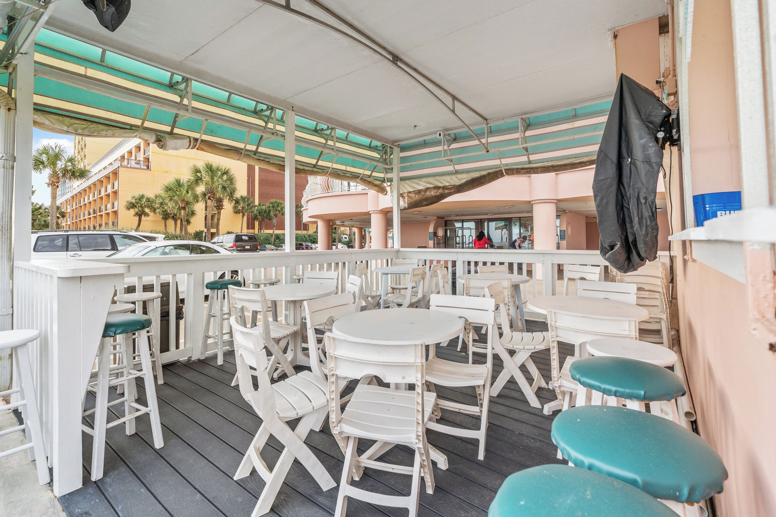 An outdoor seating area with white tables and chairs, a covered section with a striped awning, and a view of the surrounding buildings.