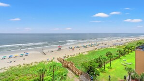 A beach with umbrellas, a wooden walkway, and a view of the ocean. - Units at St. Clements at Caravelle by Elliott Beach Rentals (Myrtle Beach)