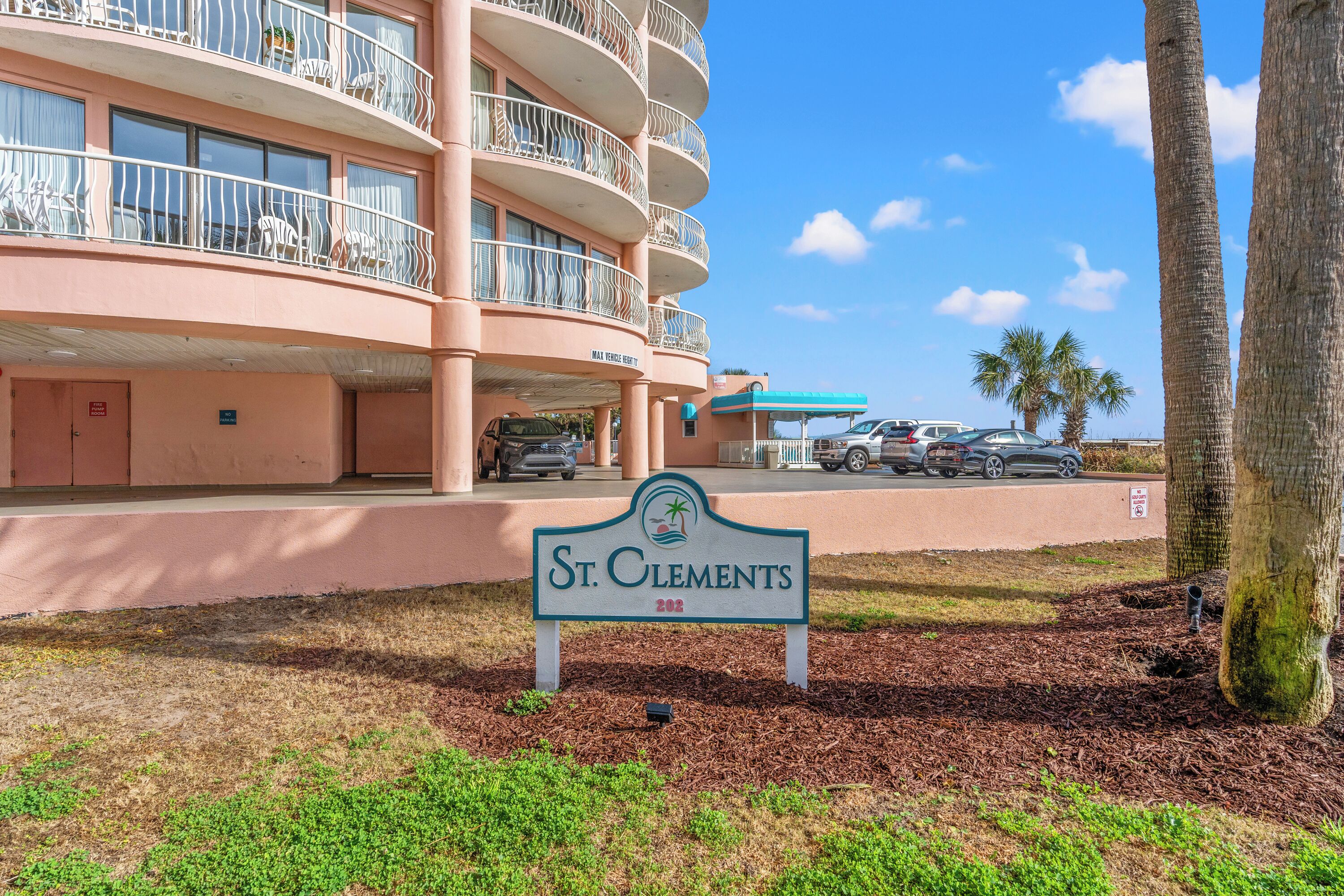 A multi-story hotel with balconies, a sign reading "St. Clements 202", and a parking area with cars.