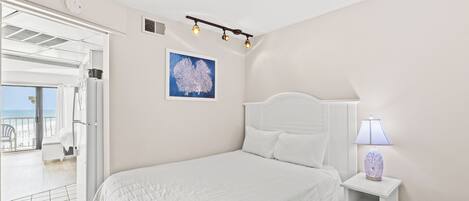 A bedroom with a bed, a nightstand with a lamp, a ceiling light fixture, and a framed artwork on the wall.