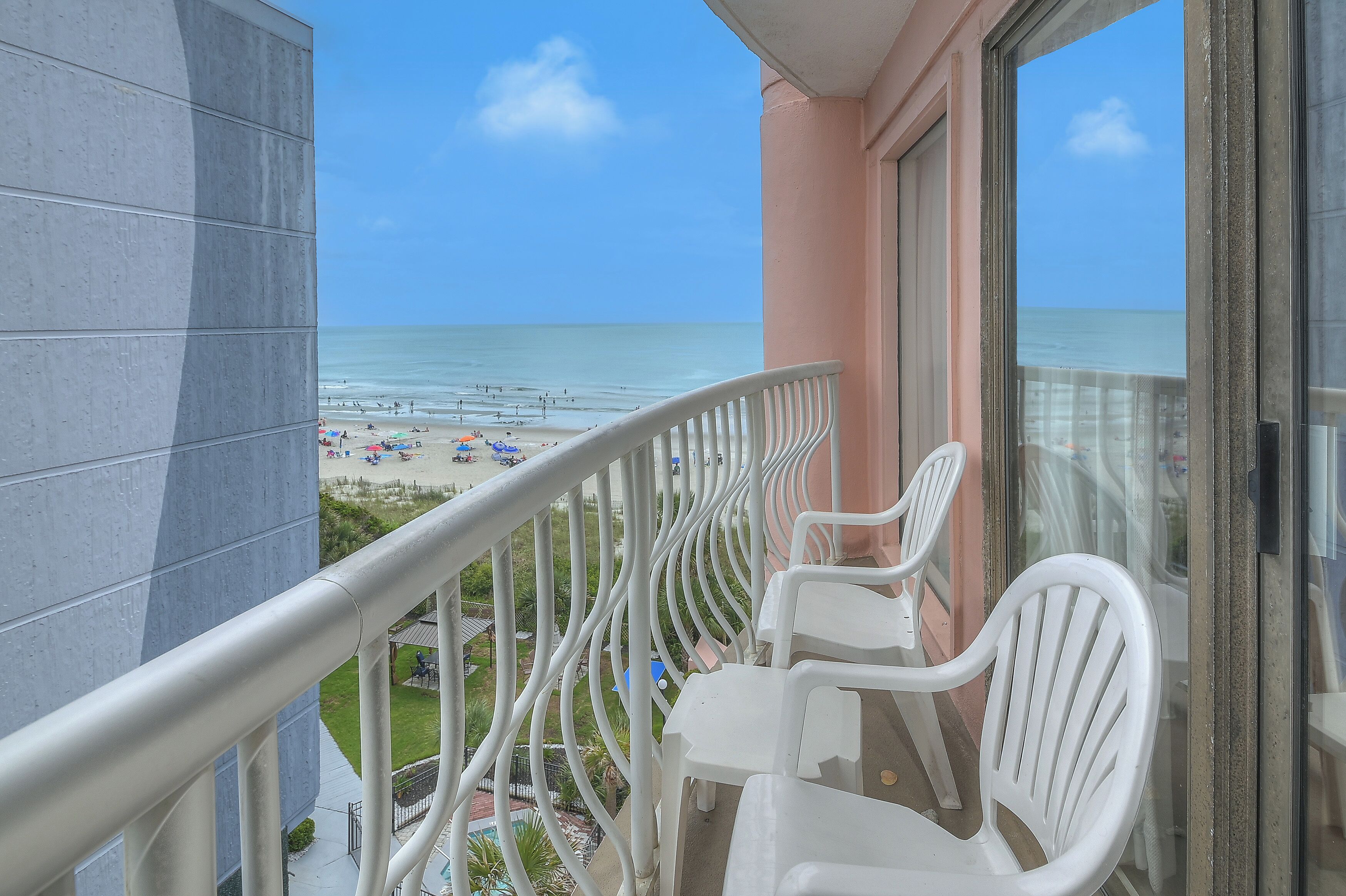 Een balkon met witte stoelen en uitzicht op het strand, onder een heldere lucht.