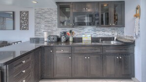 A modern kitchen with dark wood cabinets, a large island with a sink, and a microwave above the cabinets. - Units at St. Clements at Caravelle by Elliott Beach Rentals (Myrtle Beach)