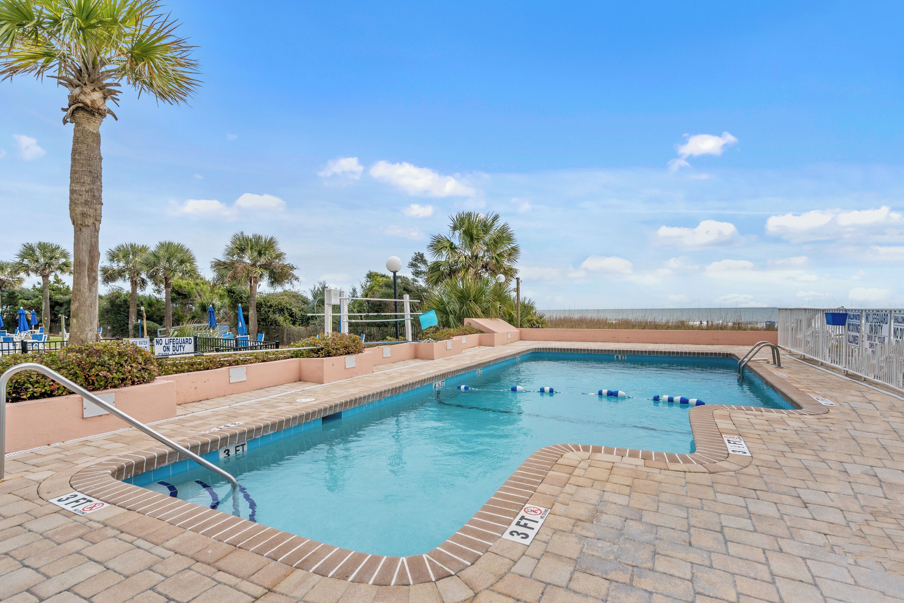 A swimming pool with clear blue water, surrounded by palm trees and a brick deck.