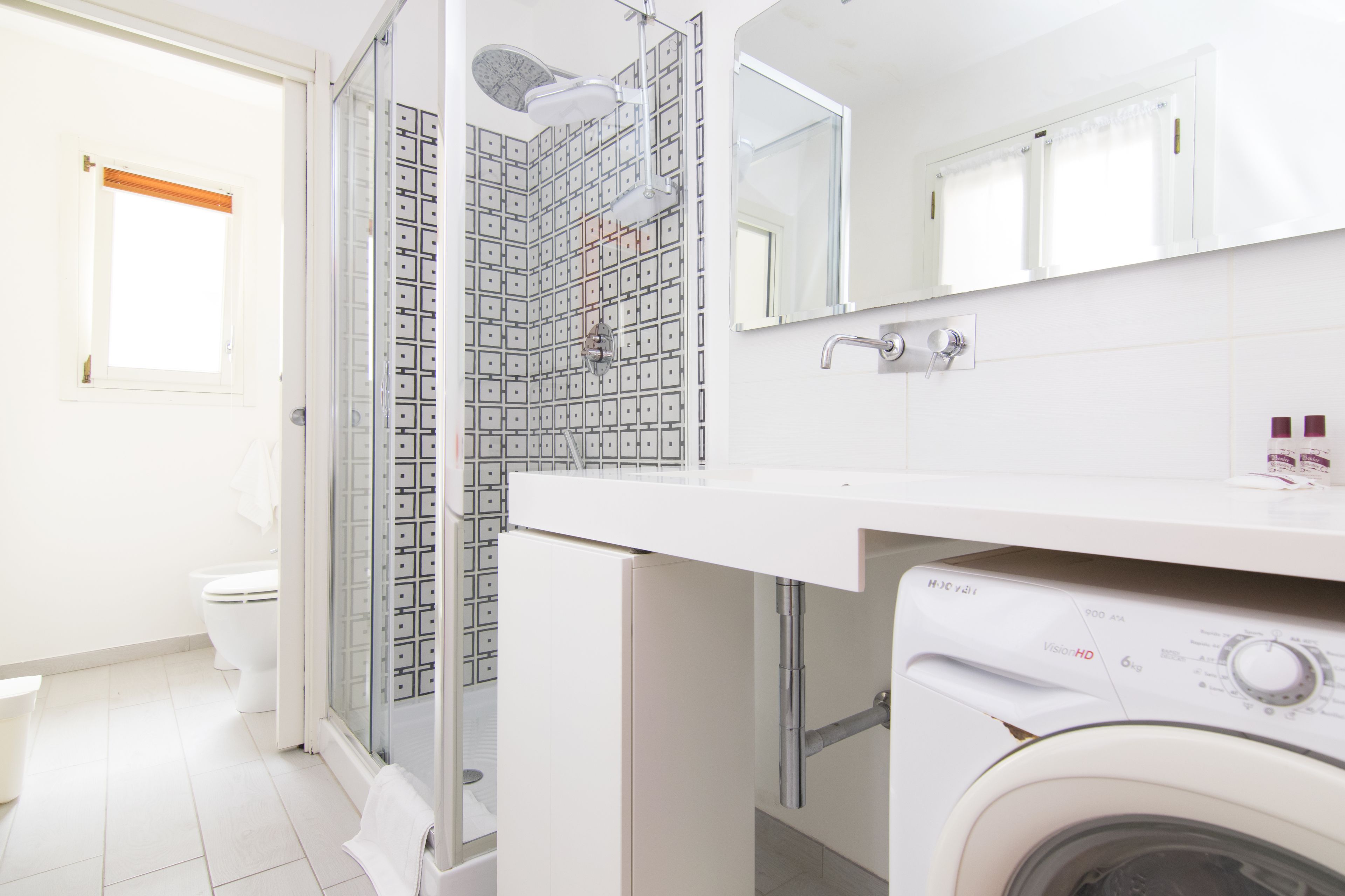 Une salle de bain moderne dotée d’une douche à parois de verre, d’un lave-linge encastré et d’un grand miroir au-dessus du lavabo.