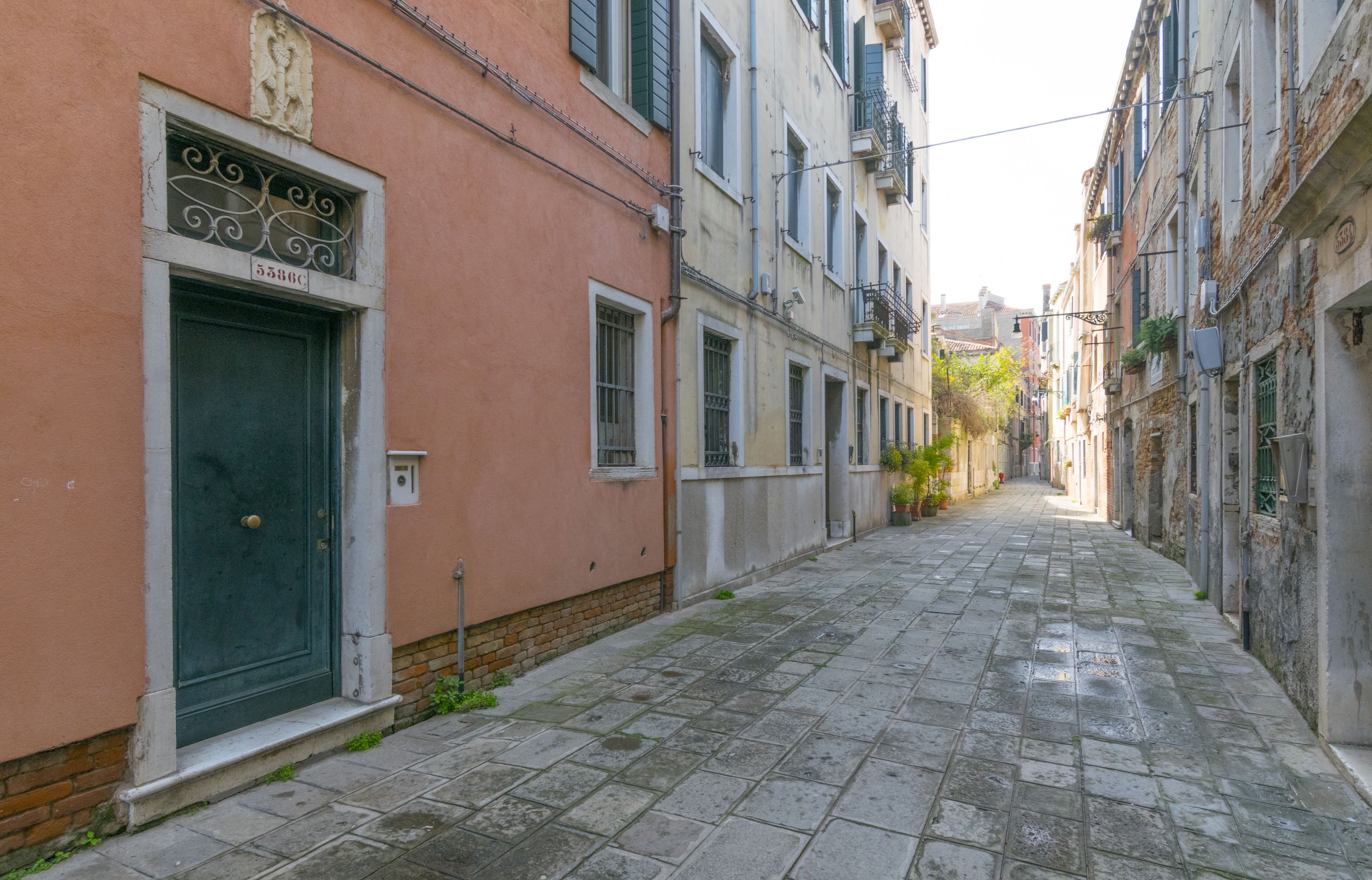 A narrow cobblestone street flanked by historic buildings with traditional balconies and a green door.