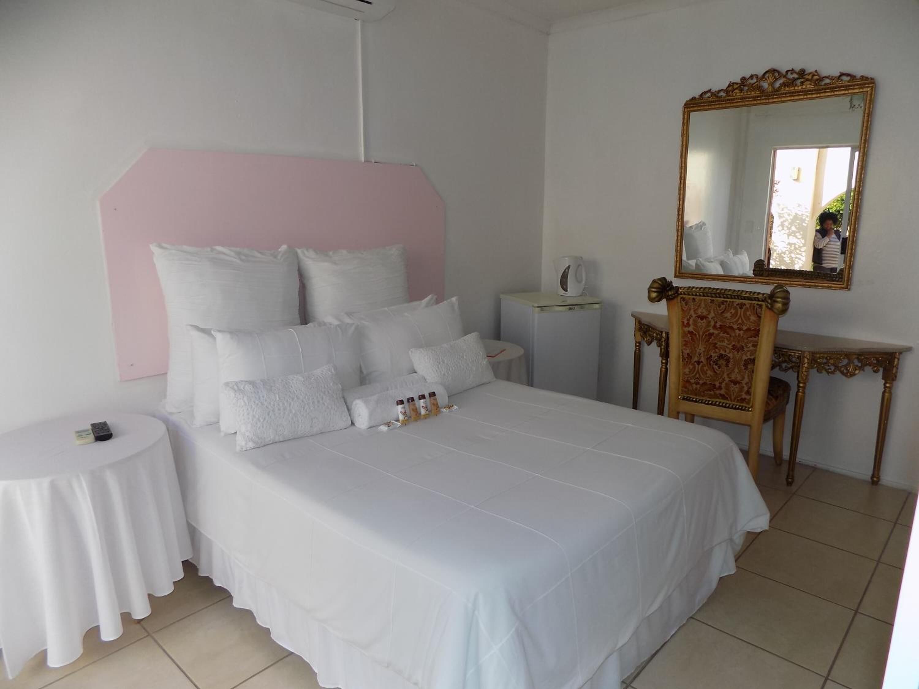 A bedroom with a large bed, a bedside table, a vanity with a mirror, and a small table with a cup.