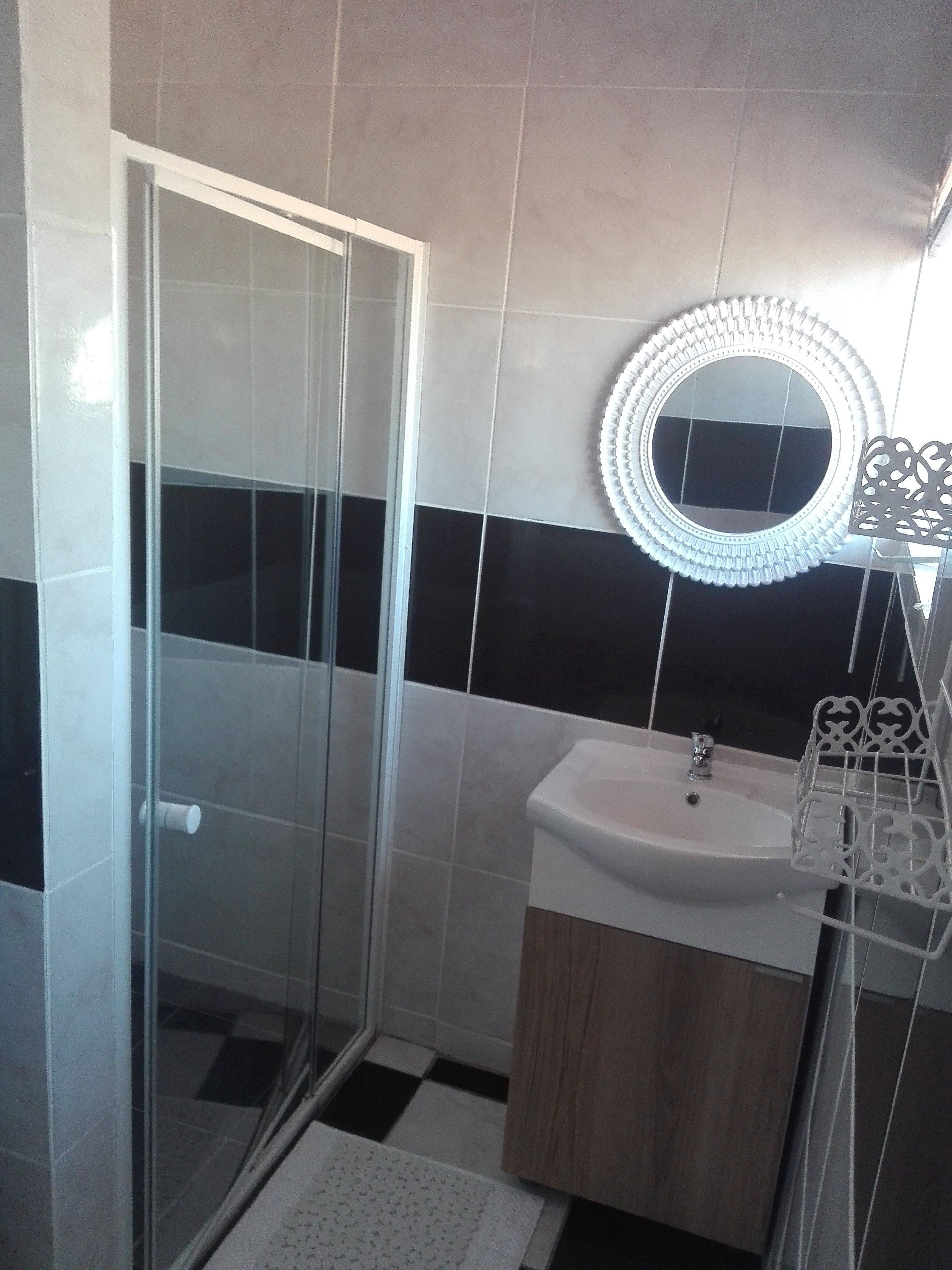 A bathroom with a glass shower enclosure, a sink with a decorative mirror, and a patterned rug.